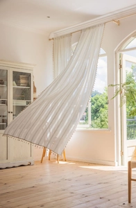Detail of off-white striped linen curtain featuring elegant ball tassel fringe at bottom