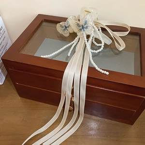 Détail de papillons brodés, de rubans crème et de glands en perles sur une pince à cheveux