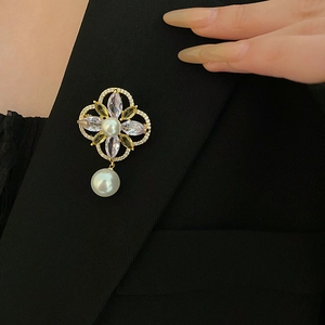 Detail of flower brooch with gold plating, zircon petals and white pearl on a suit