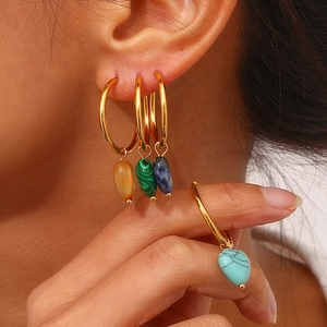Golden hoop earrings with colorful natural stone heart pendants worn by a model