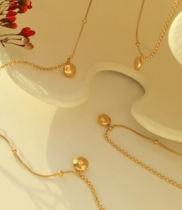 Détail d'un collier chaîne serpent dorée avec pendentif disque gravé Lucky