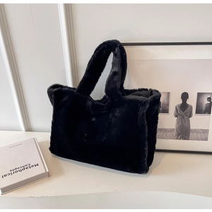 Nature morte d'un sac cabas en peluche noir posé sur un bureau avec un livre blanc