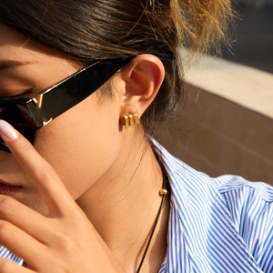 Détail de boucles d'oreilles dorées à trois couches portées par un mannequin au soleil