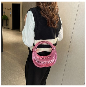 Pink crescent acrylic handbag with woven texture and gold chain on model's shoulder