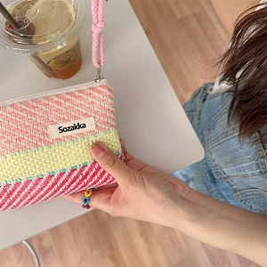 Close-up of hand-held colorful striped woven cosmetic bag with zipper and logo patch