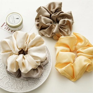 Detailed texture of large silk scrunchies in cream, brown, and yellow on a ceramic plate