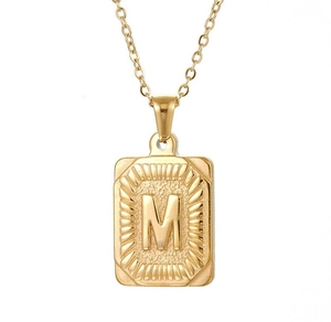 Gros plan d'un pendentif rectangulaire en or 18 carats avec lettre M et bords ciselés