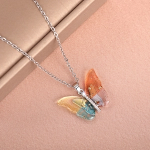 Close-up of butterfly pendant with colorful resin wings, gold foil and white zircons