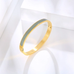 Close-up of gold stainless steel bangle with grey enamel inlay on white geometric stand