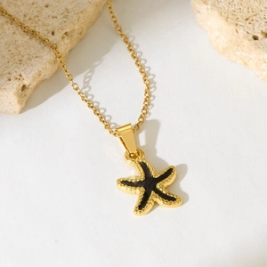 Golden starfish necklace with black enamel inlay and micro-bead texture on stone pedestal