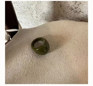 Detail shot of wide olive green resin ring on a beige linen cushion with minimalist style
