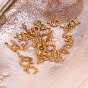 Macro shot of 18K gold-plated twisted rope texture alphabet charms on iridescent background