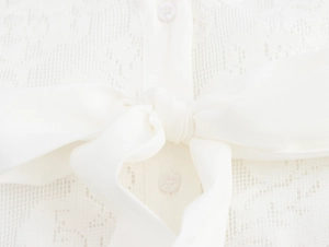 Nahaufnahme von weißem Jacquard-Stoff mit dekorativer Schleife und Knopfdetails