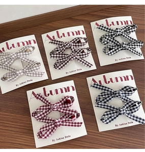 Close-up of five pairs of plaid ribbon hair clips in various colors on wooden surface