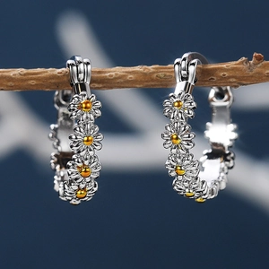 Elegant silver daisy hoop earrings with gold accents displayed on a rustic branch