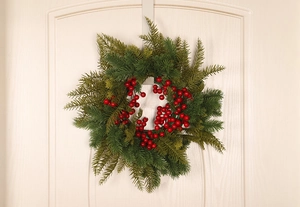 Close-up of a Christmas wreath with red berries and green pine needles on a white door