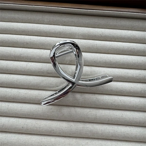 Close-up of polished silver twisted metal hair claw clip on a beige jewelry tray