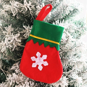 Close-up of mini red Christmas stocking with snowflake patch hanging on snowy tree