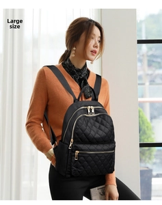 Detail of a large black quilted nylon backpack featuring elegant gold metal zippers and pockets