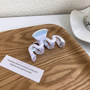 Close-up of iridescent white wavy hair claw clip on a rustic wooden decorative tray