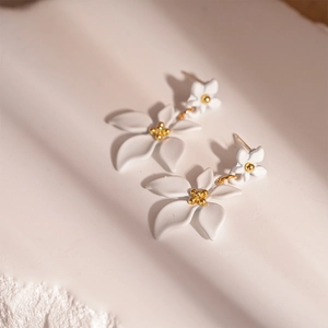 Détail de boucles d'oreilles fleurs blanches au cœur doré sur surface texturée
