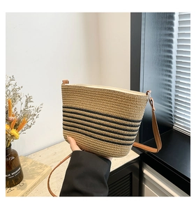 Detail of handwoven straw bucket bag with black stripes and brown leather strap