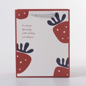Detail of red strawberry gift bag with woven handles and holiday greeting text