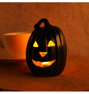 Close-up of black matte Halloween pumpkin lantern with warm orange glowing interior light