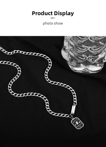 Detailed close-up of a silver nameplate necklace with 'Good Luck' engraving on dark fabric