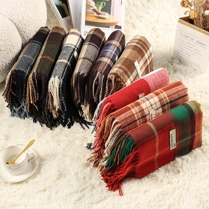 Close-up of thick plaid knit scarves with tassels and white labels on a soft white rug