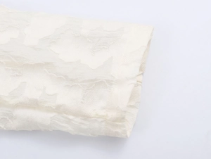 Détail du poignet d'un blazer en dentelle blanche montrant le motif et la texture plissée