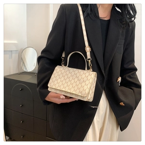 Detail of beige crossbody bag with M-pattern texture and adjustable shoulder strap