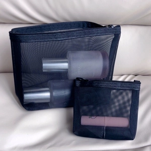 Detail of two black mesh cosmetic bags with zippers on beige wrinkled fabric background