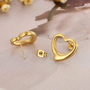 Detail view of heart-shaped gold stainless steel earrings on a beige textured surface