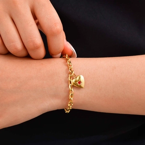 Dettaglio del bracciale con ciondolo a cuore dorato, zircone rosso e incisione
