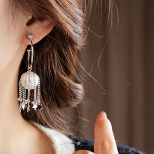 Détail de boucles d'oreilles à pompons étoiles argentées avec perles portées par un modèle