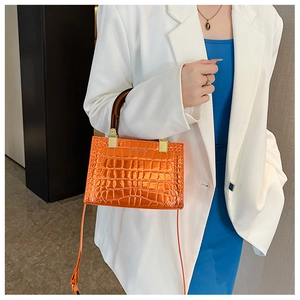 Detail of bright orange faux crocodile skin bag with bamboo handle and gold buckle