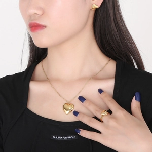 Close-up of 18K gold plated heart necklace, stud earrings, and ring set on a model