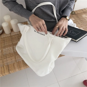 Vista de cerca de bolso tote de lona blanca con texto merciparis negro sobre banco