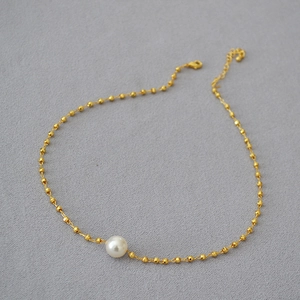 Detailed view of a gold beaded necklace featuring a white pearl pendant and lobster clasp