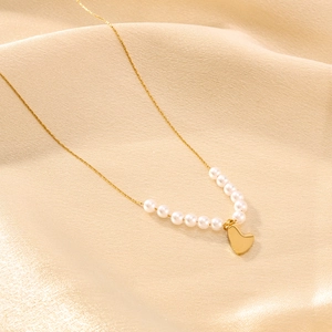 Collana in titanio dorato con cuore e perle su un elegante tessuto di seta color beige