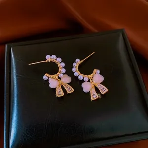 Elegant gold bow earrings with pearls and pink hearts displayed on a black leather jewelry box