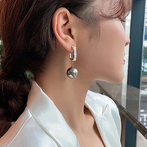 Close-up detail of a C-shaped gold earring with zircon stones and a grey faux pearl dangle