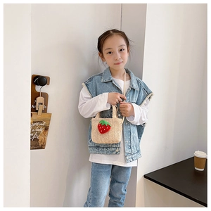 Girl wearing a beige straw bag with strawberry accents and long shoulder strap