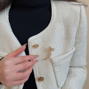 Detail of a gold flower brooch with zircon and pearl on a white tweed jacket collar