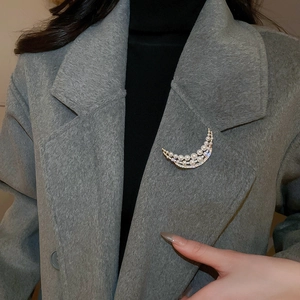 Close-up of crescent moon brooch with pearls and rhinestones on grey wool coat
