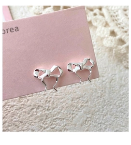 Macro shot of silver S999 bow stud earrings on a pink card with delicate white lace details