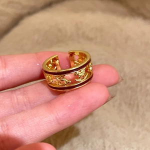 Detail of gold-plated open ring featuring hollow brand logo and red enamel inlay