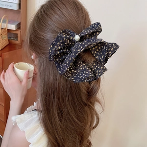 Detail of a large black polka dot bow hair scrunchie with a central pearl on hair