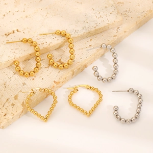 Close-up of gold and silver beaded heart and C-shaped earrings on stone tray